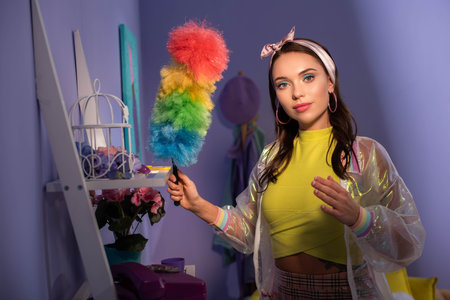 young woman posing as doll with duster at home