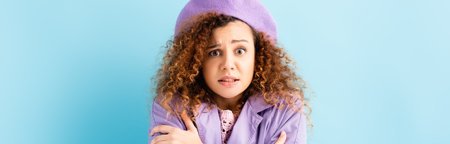 curly woman in beret freezing and embracing herself on blue background, banner