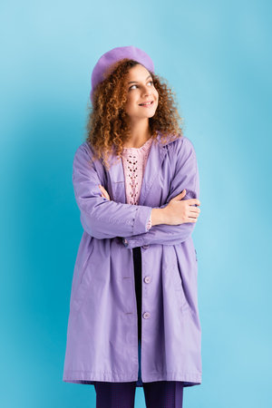 pleased young woman in beret and coat looking away on blueの写真素材