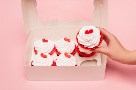 cropped view of woman holding valentines cupcake near box on pink backgroundの写真素材