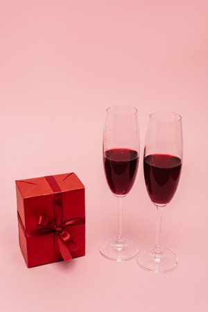 red wine in glasses near gift isolated on pinkの写真素材
