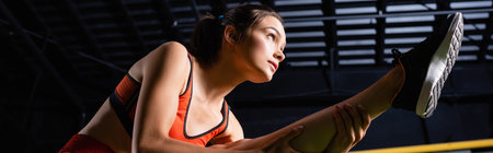 athletic woman in sports top stretching leg while training in gym, banner