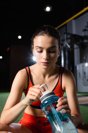 thirsty sportswoman opening sports bottle in gym