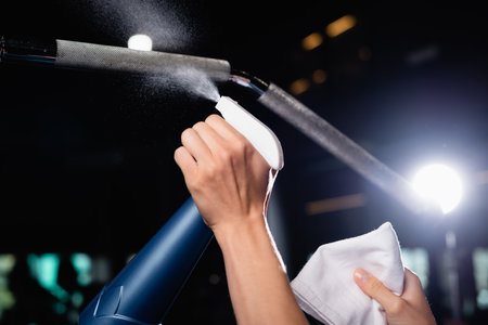partial view of charwoman spraying detergent on sports equipment in gymの写真素材