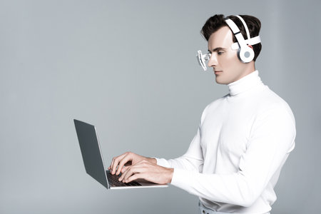 Cyborg in headphones and eye lens using laptop in air isolated on grayの写真素材