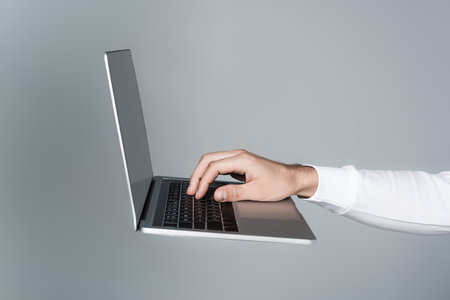 Cropped view of man using laptop with blank screen in air isolated on gray
