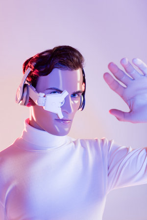 Cyborg man in eye lens and headphones looking at hand on blurred foreground on purple background