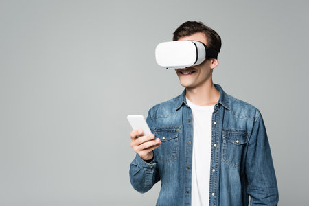 Smiling man vr headset using smartphone isolated on grayの写真素材