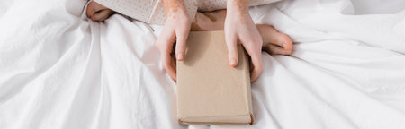 cropped view of woman with vitiligo holding book in bedroom, bannerの写真素材