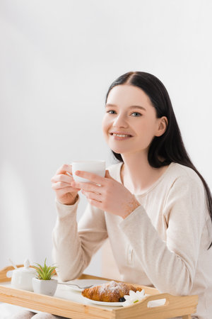 happy woman with vitiligo holding cup of tea near breakfast on trayの写真素材