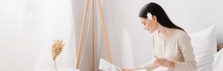 happy woman with vitiligo and flower in hair holding cup and reading newspaper, bannerの写真素材