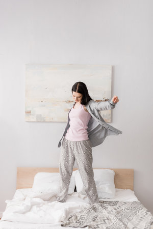 full length of happy woman with vitiligo stretching while standing on bedの写真素材