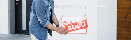 Cropped view of man holding sign with sold lettering near house, bannerの写真素材