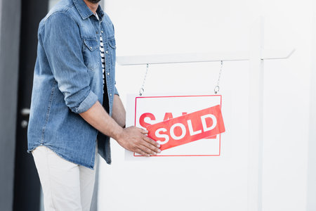 Cropped view of man holding sign with sold lettering near house on blurred backgroundの写真素材