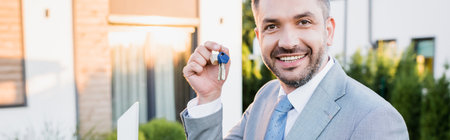 Portrait of happy real estate agent showing keys while looking at camera on blurred background, bannerの写真素材
