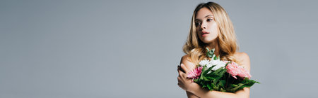 charming young woman with naked shoulders posing with bouquet isolated on gray, bannerの写真素材
