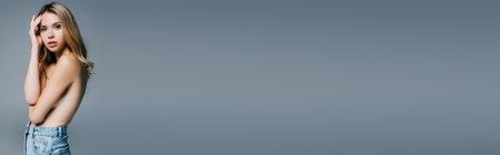 seductive topless woman in jeans hiding breasts with hands isolated on gray, bannerの写真素材