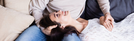 Smiling woman looking at boyfriend while holding hands on couch, bannerの写真素材