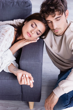 Young woman with closed eyes lying on couch near boyfriend at homeの写真素材