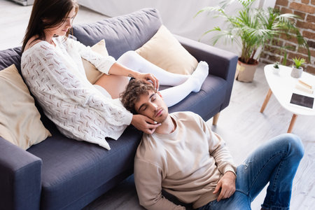 Young woman touching face of boyfriend while siting on sofa at home