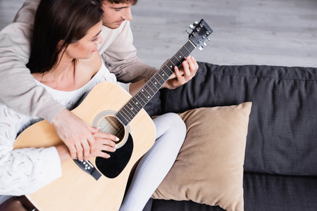 High angle view of young man teaching girlfriend to playing acoustic guitar at home