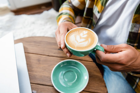cropped view of man sitting in cafe and holding cup of coffee with latte artの写真素材