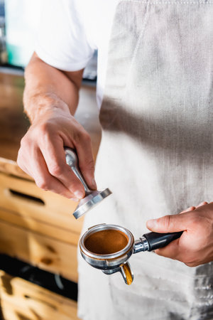 cropped view of barista holding press and portafilter with roasted ground coffeeの写真素材