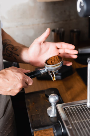 cropped view of tattooed barista holding portafilter with roasted ground coffeeの写真素材