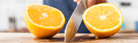 Close up view of halves of juicy orange near knife in hand of man on blurred background, banner