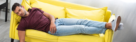 Young man sleeping on yellow couch at home, bannerの写真素材
