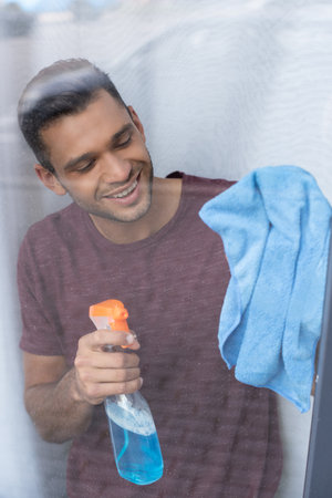 Smiling man cleaning glass of window with detergent and ragの写真素材