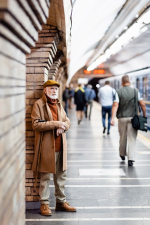 aged man in autumn outfit standing near people and train on metro platform on blurred foregroundの写真素材