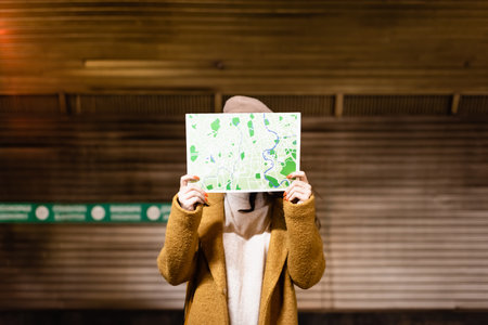 woman in autumn coat obscuring face with city map at subway stationの写真素材