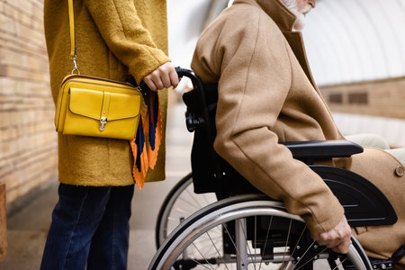 cropped view of woman holding wheelchair of senior disabled man on metro stationの写真素材