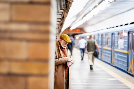 senior man in autumn coat and cap standing on underground platform on blurred foregroundの写真素材