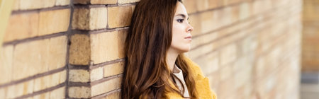 thoughtful woman leaning on brick wall while standing at metro station on blurred background, bannerの写真素材