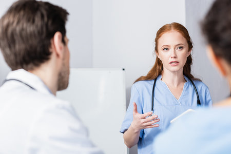 Nurse with digital tablet talking to colleagues on blurred foreground in clinicの写真素材