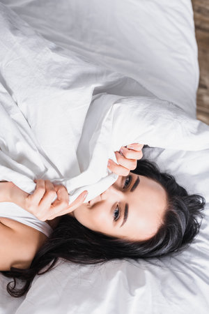 top view of young brunette woman in bed under blanketの写真素材