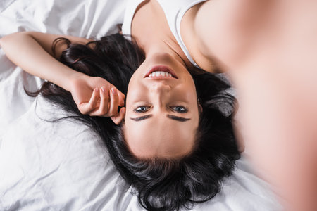 top view of young smiling brunette woman lying in bedの写真素材