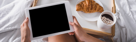 cropped view of woman having growing and cocoa for breakfast while holding digital tablet in bed, bannerの写真素材