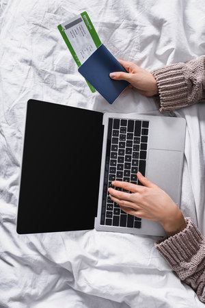 top view of woman in sweater lying in bed with laptop and air ticketの写真素材