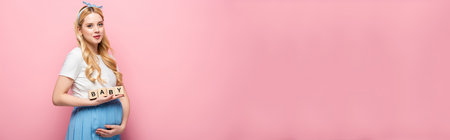 blonde young pregnant woman holding cubes with baby lettering on pink background, bannerの写真素材