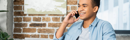 happy african american man looking away while talking on smartphone, banner