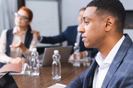 Side view of african american businessman near blurred colleagues on background in boardroom