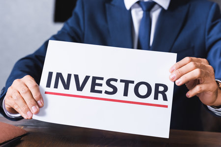 Cropped view of businessman holding sign with investor lettering in meeting room on blurred backgroundの写真素材