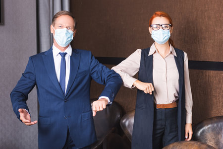 Businesspeople in medical masks looking at camera while greeting each other with elbows in meeting roomの写真素材