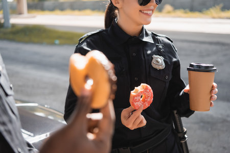 cropped view of policewoman with donut and paper cup on blurred foreground outdoorsの写真素材