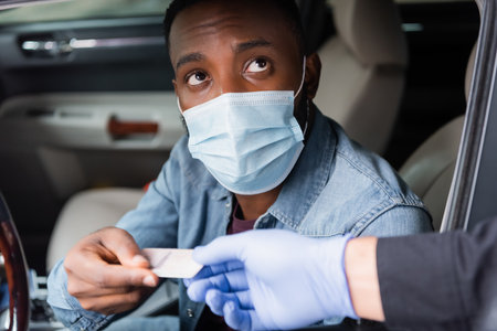 African american driver in medical mask giving license to policeman on blurred foreground near carの写真素材