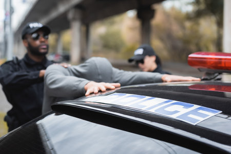 patrol car with blue police lettering near multicultural enforce law officers arresting offender on...