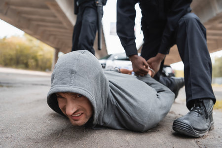 african american policeman handcuffing offender lying on street on blurred background outdoorsの写真素材